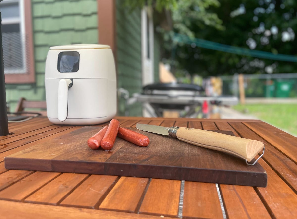 hot dogs lie in a pile on an outdoor table next to white air fryer