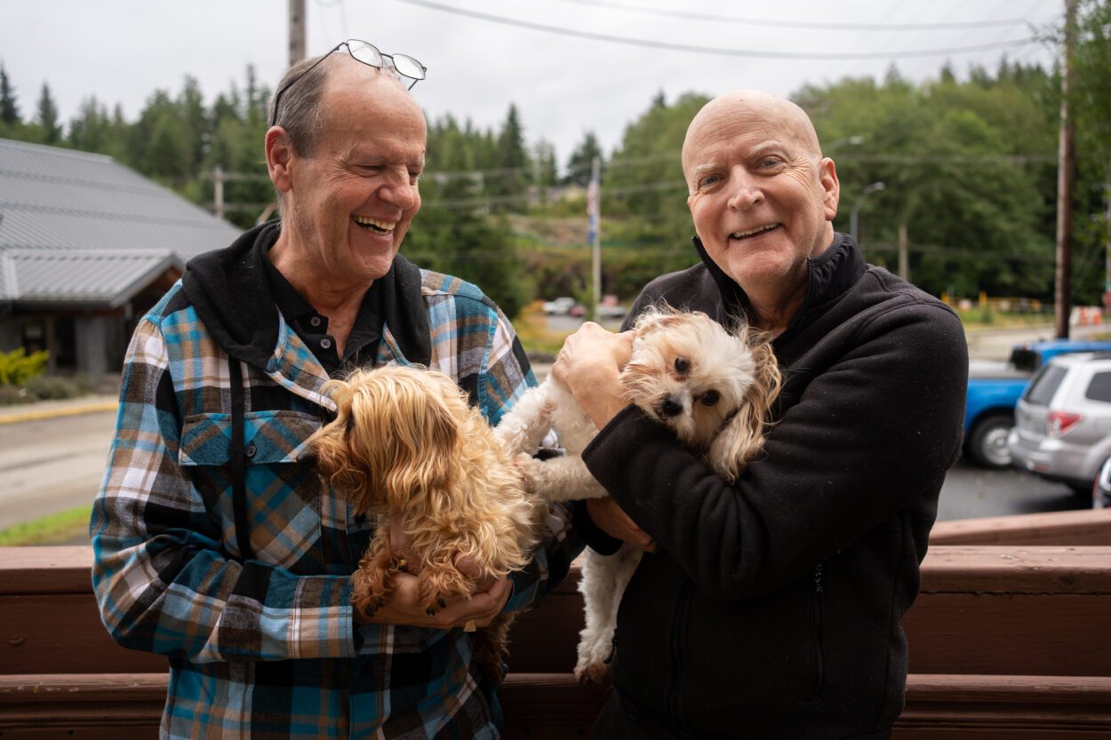 two men smiling and each holding a small dog