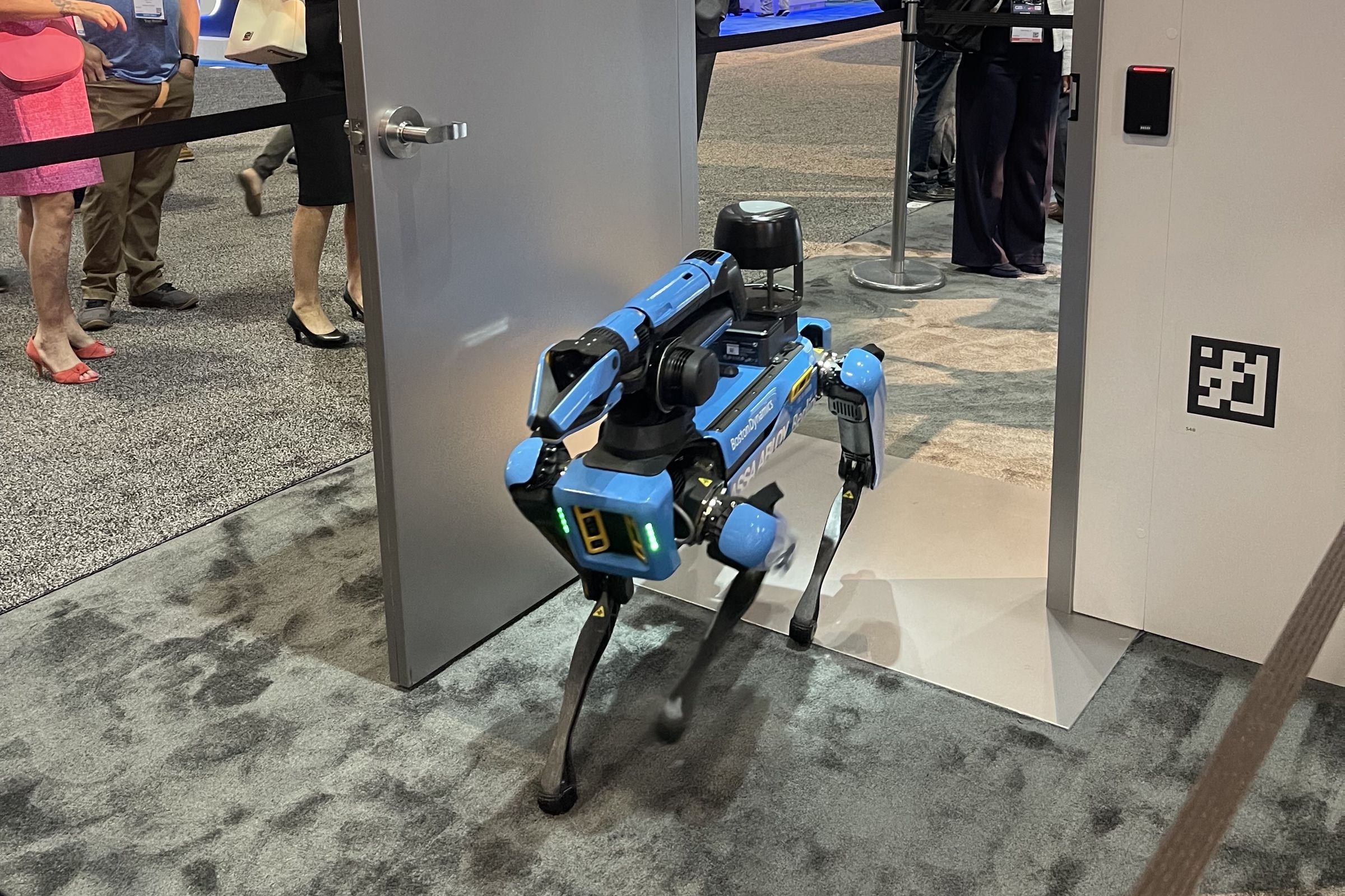 blue robot dog entering a door with an access panel on the wall and a QR code.