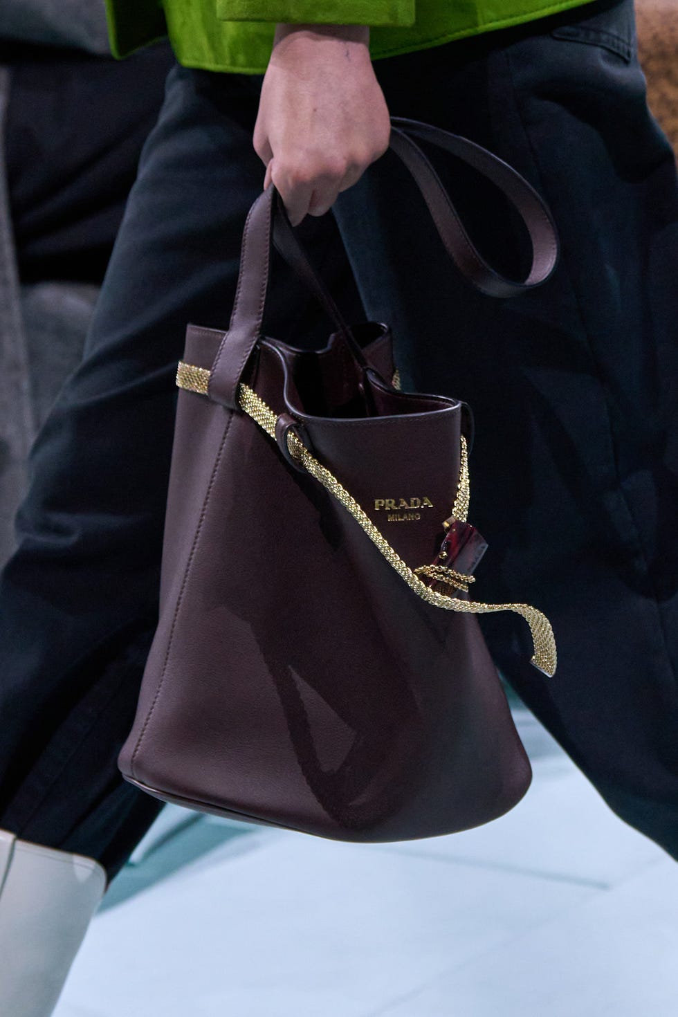 Fashion model holding a brown bucket bag with a gold chain detail