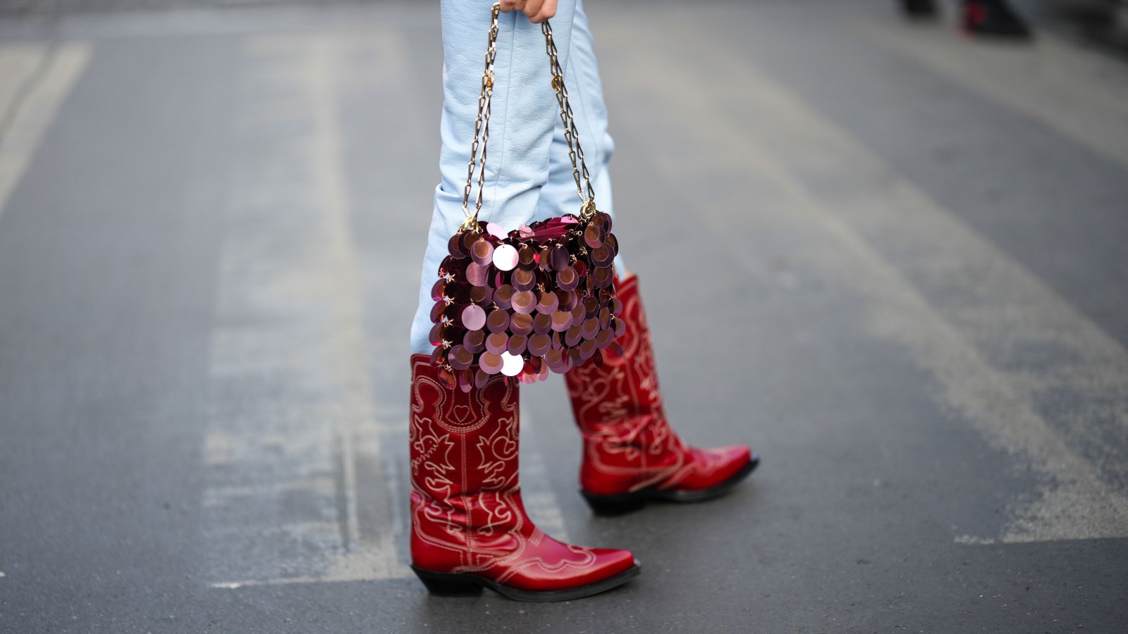 PARIS, FRANCE - MARCH 01: A guest wears pale blue shiny leather skinny pants, a burgundy coins handbag from Paco Rabanne, red shiny leather with embroidered white pattern pointed block heels knees boots , outside Cecilie Bahnsen, during Paris Fashion Week - Womenswear Fall Winter 2023 2024, on March 01, 2023 in Paris, France. (Photo by Edward Berthelot/Getty Images)