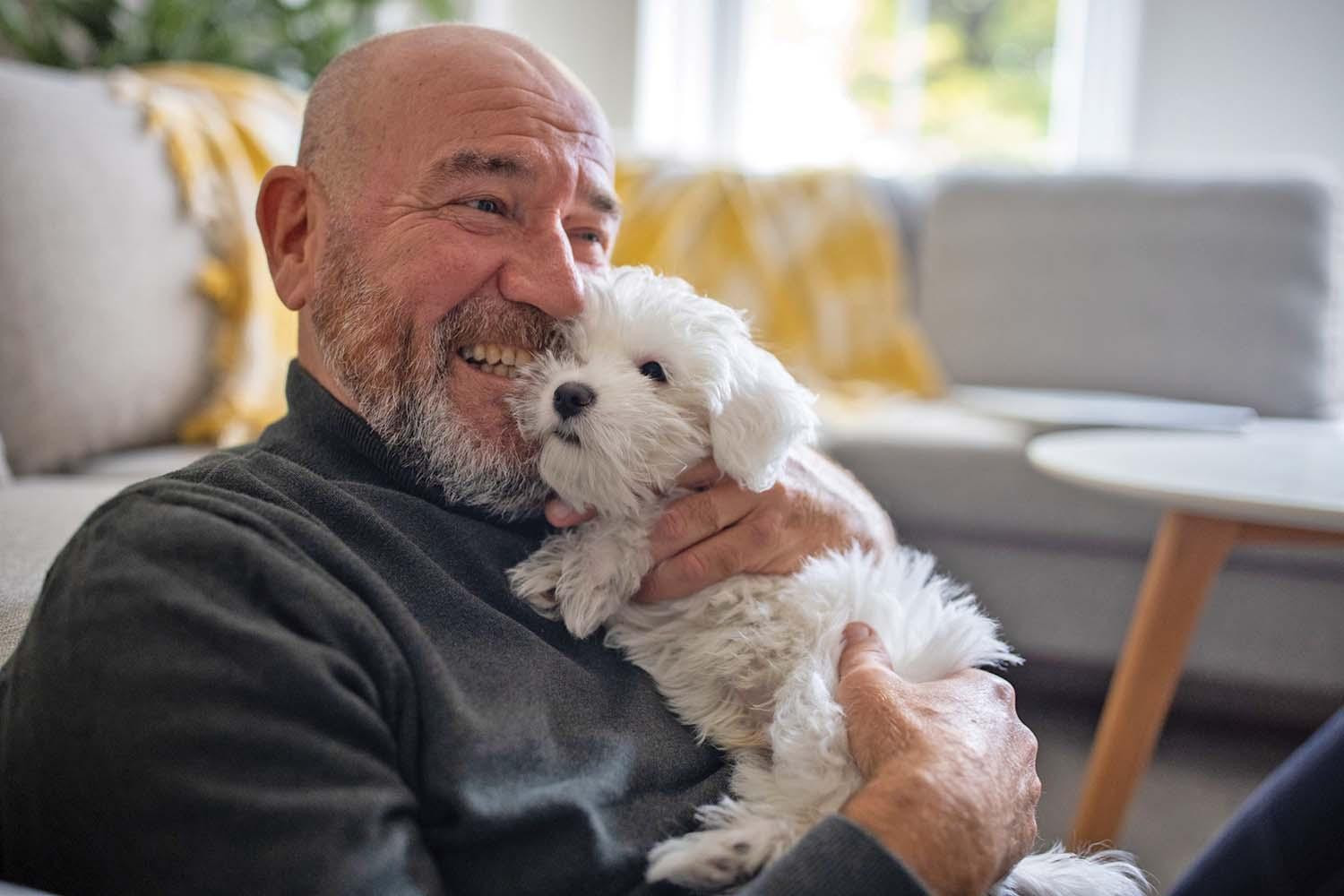 A smiling man holds a fluffy white puppy.