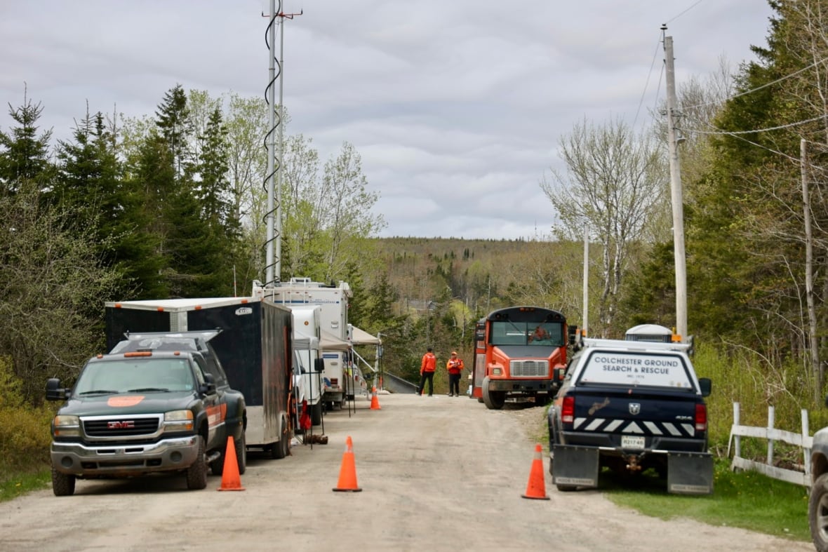 A number of search and rescue vehicles line a dirt road with woods in the background.