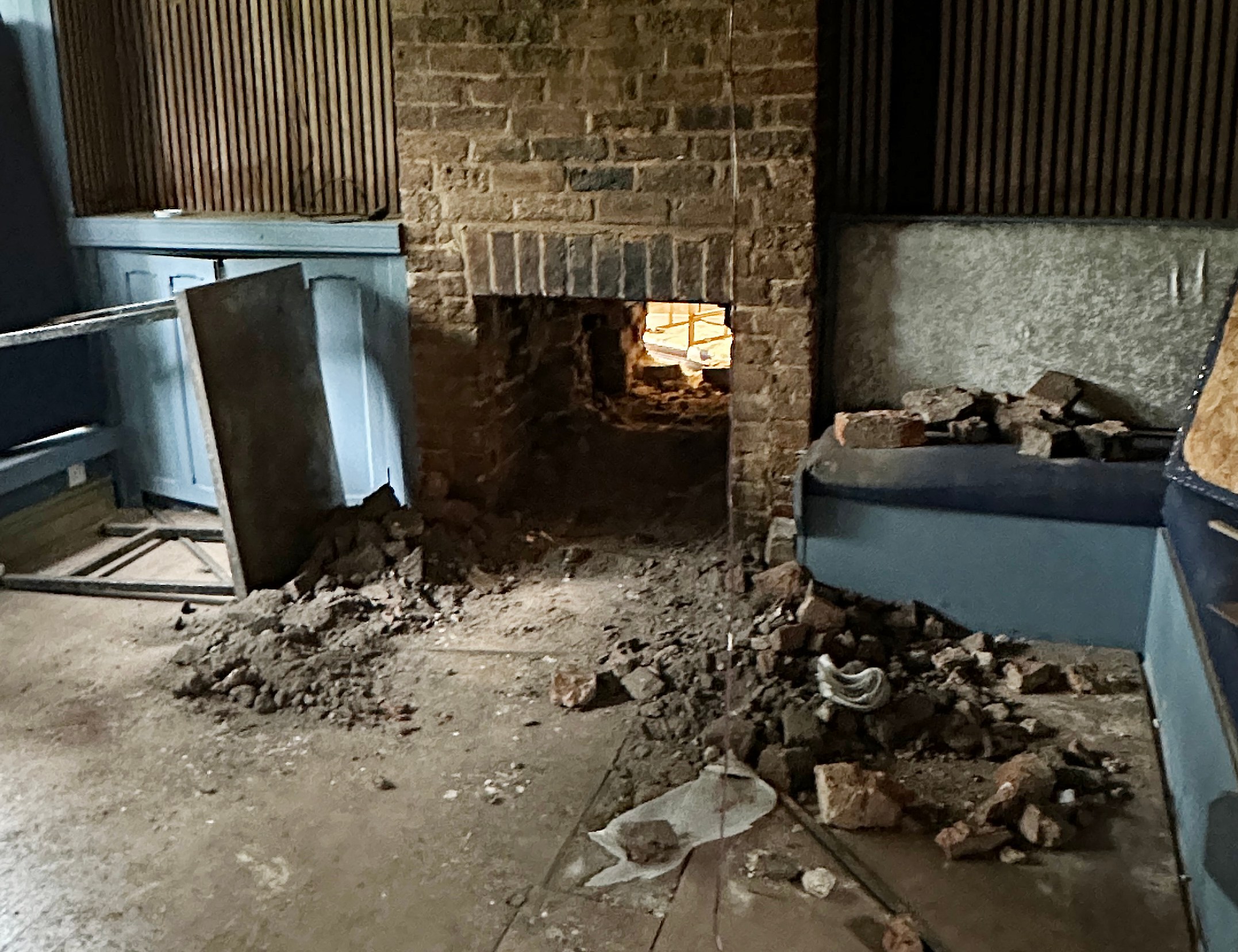 Damaged room interior with a broken fireplace and debris on the floor.